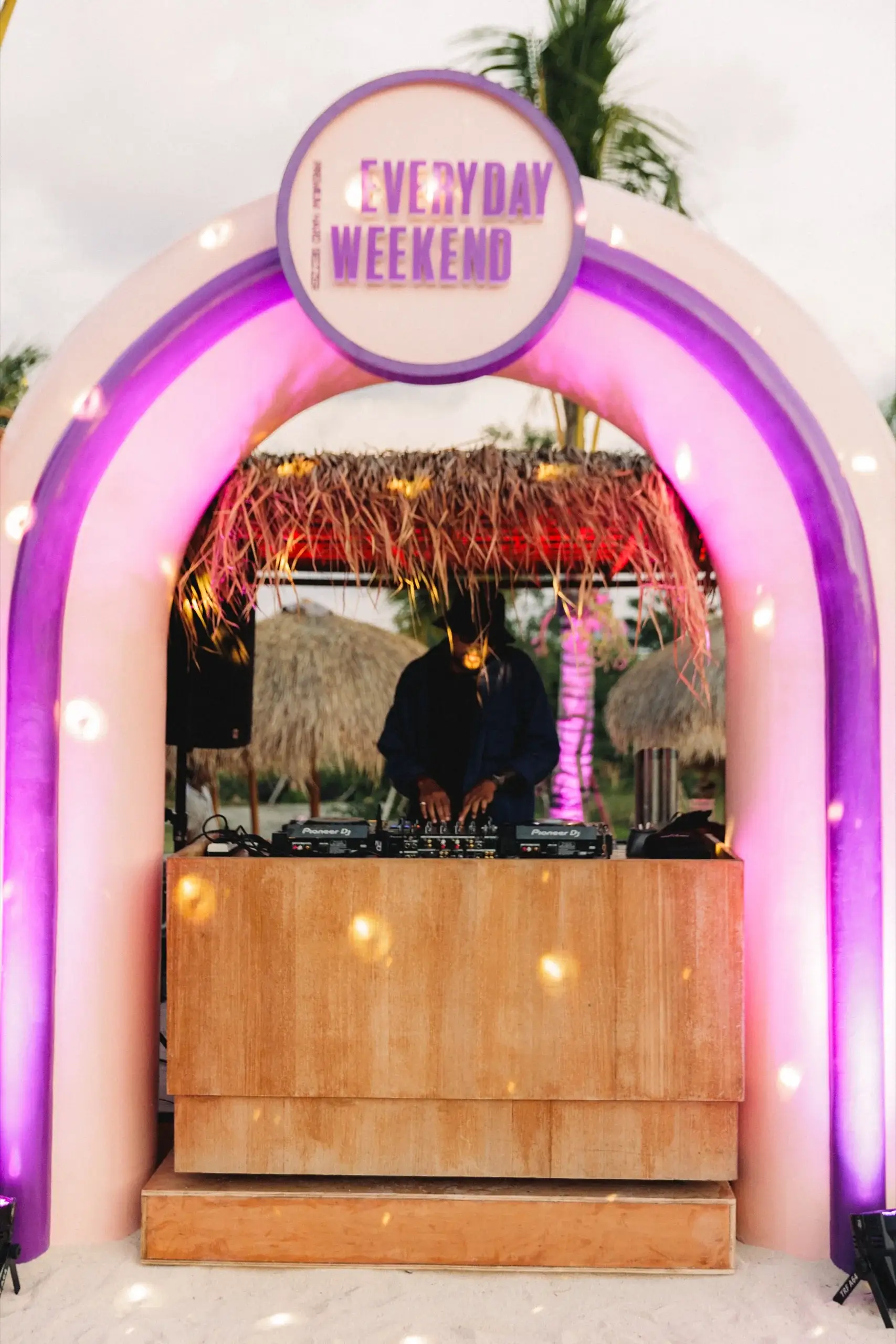 Booth DJ di dalam lengkung berlampu merah muda dengan papan EVERYDAY WEEKEND menyala di atasnya