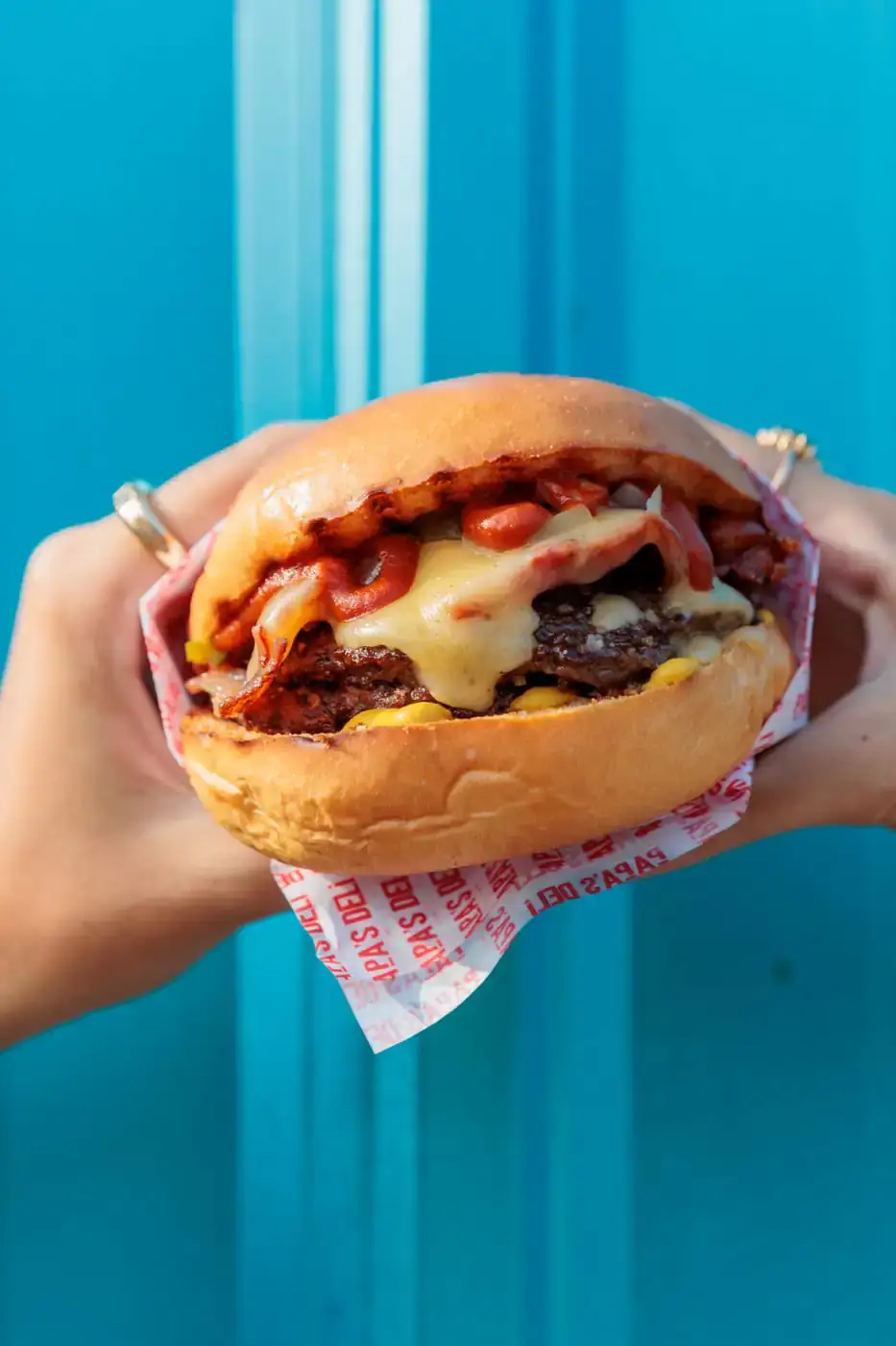 Burger dalam bungkusnya di depan dinding sian cerah