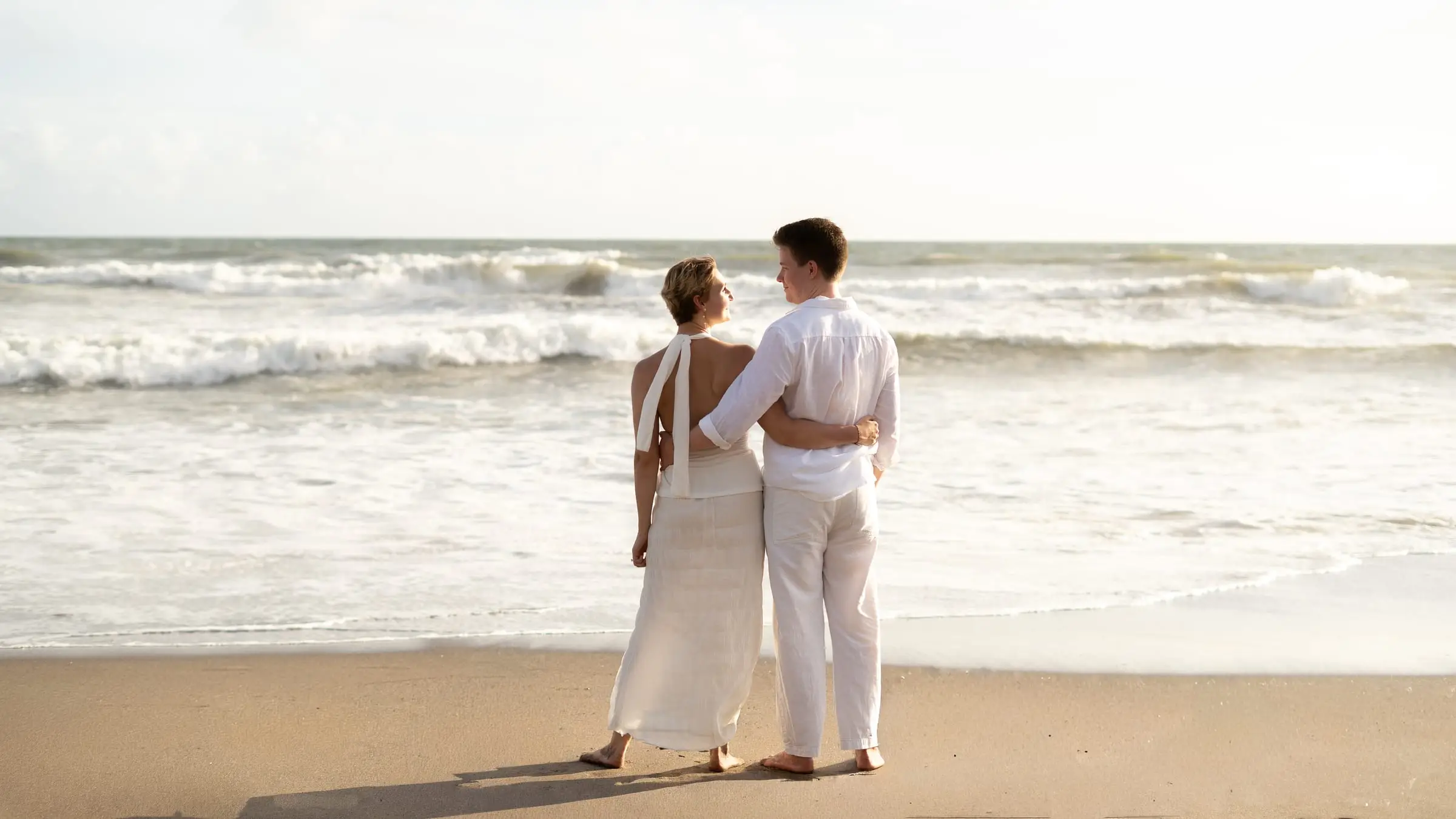 Couple in white standing and looking out to sea